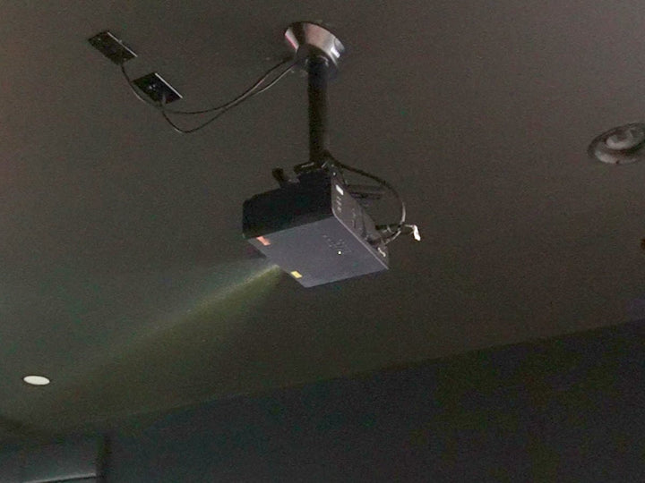 Ceiling-mounted golf simulator projector on its mount, beam lit