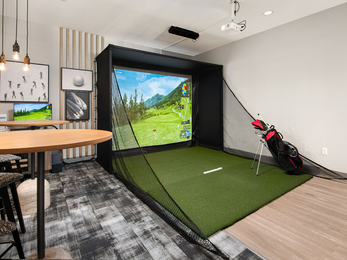 Golf simulator enclosure in a modern lounge with a ceiling-mounted projector and high-top seating